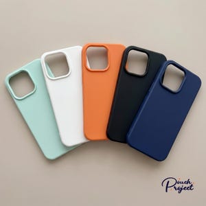 May include: A collection of five colorful phone cases in mint green, white, orange, black, and navy blue. Each case has a camera cutout and a smooth, matte finish. The cases are arranged in a fan shape.