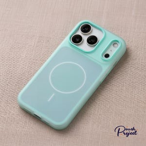 Pu&ograve; includere: Una custodia per telefono verde acqua chiaro con retro trasparente e cerchio MagSafe bianco. La custodia ha un paraurti protettivo attorno agli obiettivi della fotocamera e una cornice verde acqua abbinata.