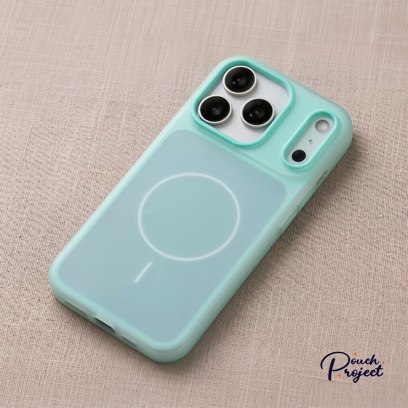 Pu&ograve; includere: Una custodia per telefono verde acqua chiaro con retro trasparente e cerchio MagSafe bianco. La custodia ha un paraurti protettivo attorno agli obiettivi della fotocamera e una cornice verde acqua abbinata.