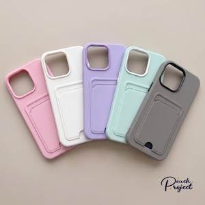 Könnte beinhalten: Fünf Smartphone-Hüllen in Fächerform angeordnet, mit integriertem Kartenfach auf der Rückseite. Die Farben sind Pink, Weiß, Lavendel, Mintgrün und Grau. Jede Hülle hat einen quadratischen Kameraausschnitt und den Text Pouch Project.
