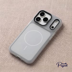 Pu&ograve; includere: Una custodia per telefono grigia trasparente con una cornice nera per la fotocamera e un cerchio bianco sul retro. La custodia ha un design elegante e moderno ed &egrave; realizzata in materiale resistente. Protegge il telefono da graffi e danni.