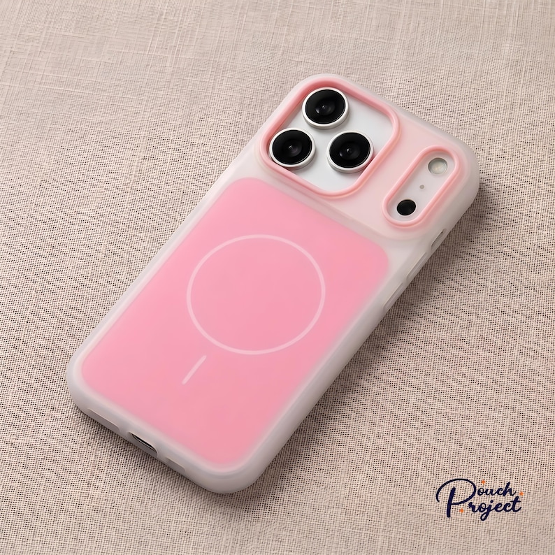 Pu&ograve; includere: Una custodia per telefono rosa e bianca con design MagSafe. La custodia ha un retro rosa con un cerchio bianco e una piccola linea e un bordo bianco. L'area della fotocamera ha tre lenti nere e un bordo rosa.