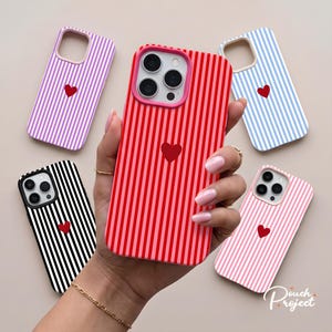 Peut inclure: Cinq coques de smartphone avec des rayures verticales et un petit cœur rouge au centre. Les coques sont disponibles en violet, rouge, bleu, noir et rose. Chaque coque possède une découpe pour l'appareil photo et un bord surélevé.