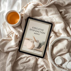 Pu&ograve; includere: Un tablet che mostra "EXECUTIVE DYSFUNCTION MENU" &egrave; appoggiato su una coperta beige, accanto a una tazza bianca piena di t&egrave; e cuffie bianche. Lo schermo del tablet mostra un design d'interni minimalista con toni neutri e dettagli in legno.