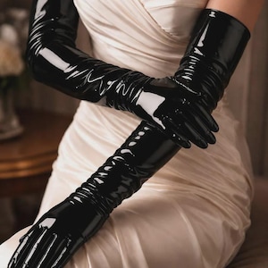 Peut inclure: Une paire de longs gants noirs brillants de style opéra, fabriqués dans une matière lisse et réfléchissante. Les gants montent bien au-dessus des coudes et présentent une coupe ajustée avec de légers plis horizontaux sur les avant-bras.