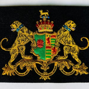 May include: Embroidered patch featuring a heraldic crest with two golden leopards flanking a shield. The shield is green with red and gold details, topped with a crown and a small dog. The patch is on a black background.