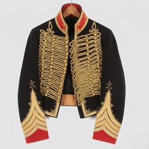 Puede incluir: Chaqueta militar negra con detalles dorados. La chaqueta presenta bordados de cuerda dorada, botones dorados y detalles rojos en el cuello y los puños. Colgada en una percha de madera.