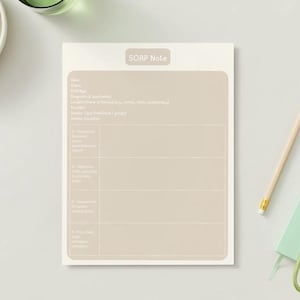 May include: A beige SOAP Note pad with a light brown rectangular section for writing. A wooden pencil, a small green notebook, and a set of keys are next to the pad. A small bowl of green grapes and a glass of water are in the background.