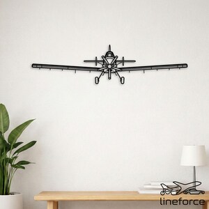 Könnte beinhalten: Schwarze Metall-Wandkunst eines Flugzeugs. Das Flugzeug hat einen Propeller, Flügel und ein Heck. Die Wandkunst ist an einer weißen Wand über einem Holztisch angebracht. Das Wort "lineforce" ist unten rechts aufgedruckt.
