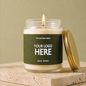 May include: A lit soy wax candle in a clear glass jar with a dark green label featuring the text 100% SOY WAX CANDLE, YOUR LOGO HERE, and BEACH RETREAT. A gold-colored metal lid rests beside the jar, which contains white wax.