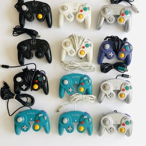 Peut inclure: Une collection de douze manettes de jeu vidéo filaires disposées en grille. Les manettes présentent diverses couleurs, dont le noir, le blanc, l'argent, le violet et le bleu sarcelle, chacune avec un stick analogique central, des boutons et un câble.