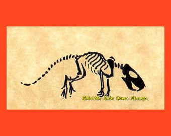 May include: A black and white illustration of a rodent skeleton on a tan background, set against an orange border. The skeleton is stylized, with visible ribs, spine, and skull. The text "Butter Side Down Stamps" is in the lower right corner.