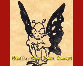 May include: Black and white illustration of a creature with wings, resembling a butterfly, and a skull-like face. The creature is sitting with its wings spread out. The image is from Butter Side Down Stamps.