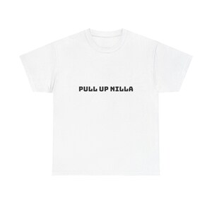 May include: A white short-sleeved t-shirt featuring the text PULL UP NILLA printed in a bold, black, block-style font across the center of the chest. The garment has a standard crew neckline and a simple, clean design with short sleeves.