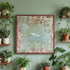 May include: Abstract painting with a textured, muted green and brown background. Two white birds are depicted in flight over a body of water. The artwork is framed in a dark brown wooden frame, creating a nature-inspired aesthetic.
