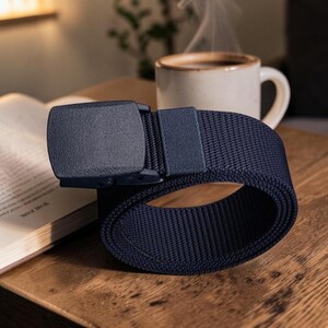 May include: A navy blue webbed belt featuring a matching navy blue rectangular buckle with a smooth, matte finish. The belt is constructed from a durable, woven nylon-like fabric and includes a coordinating fabric loop to secure the strap end.