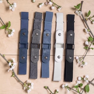 Può includere: Cinque cinture elastiche in blu navy, grigio antracite, azzurro, bianco e nero. Ogni cintura presenta una fibbia di regolazione rettangolare in metallo e una linguetta centrale verticale fissata con due bottoni a pressione in metallo.