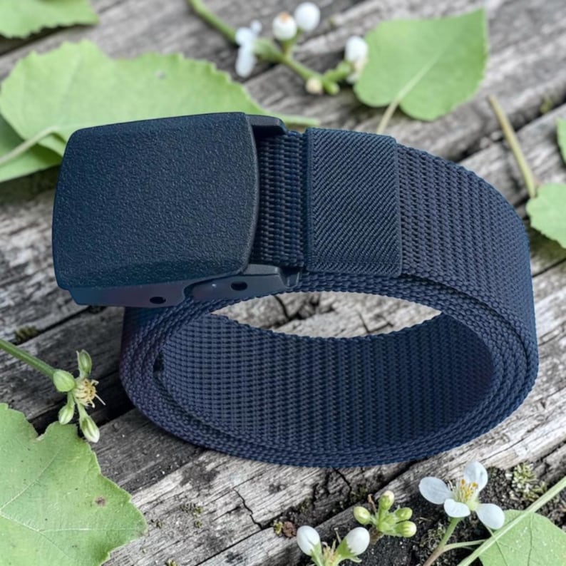 May include: A dark navy blue webbed belt featuring a solid, textured, rectangular plastic buckle. The belt strap is constructed from a durable, woven nylon material with a consistent grid pattern throughout the length of the strap.