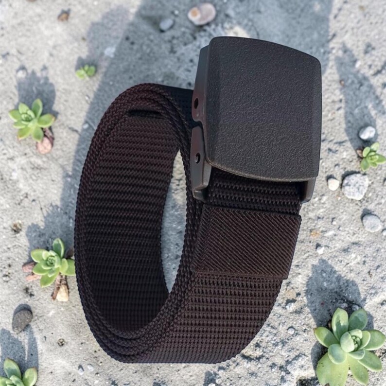 May include: A dark brown woven nylon belt featuring a matching dark brown plastic buckle with a rectangular shape. The belt strap has a textured, ribbed surface pattern and is coiled into a loop, showcasing the durable material and hardware.