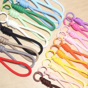 May include: A collection of colorful paracord lanyards, each featuring a woven loop attached to a matching plastic circular clasp. The set includes various solid colors such as red, black, white, green, blue, yellow, orange, pink, and brown.