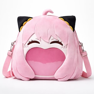 May include: Pink plush backpack shaped like a cartoon character's face, featuring black ears with yellow trim, a white face, and a large pink heart-shaped opening. The bag has a pink adjustable shoulder strap and silver-colored hardware.