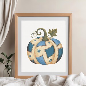 Könnte beinhalten: Ein Kreuzstichmuster eines Kürbisses mit einem Patchwork-Design in Blau- und Cremetönen. Der Kürbis hat einen grünen Stiel, eine Ranke und ein Blatt, wobei kleine blaue Blumenakzente auf die cremefarbenen Abschnitte gestickt sind.