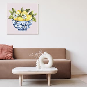May include: A watercolour painting of a bowl filled with lemons, blossoms, and green leaves. The bowl is blue and white, with a decorative pattern. The artwork is displayed on a pink background.