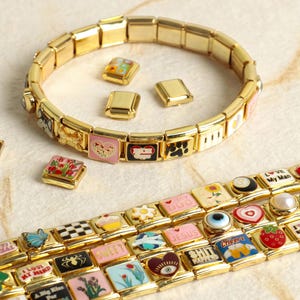May include: Gold charm bracelets with decorative charms. Charms feature hearts, flowers, and text such as "I Love My Girlfriend" and "Sweet". The bracelets are shown on a light-coloured surface.