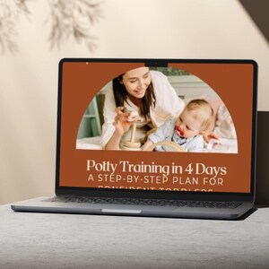 Puede incluir: Un portátil abierto muestra el texto "Potty Training in 4 Days" y una imagen de una madre y un bebé. El portátil está sobre una superficie gris claro, con un fondo neutro.