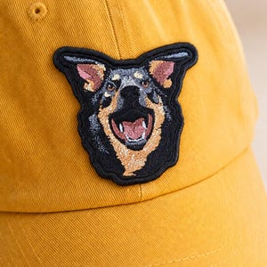 Op de afbeelding: Mosterdgele baseballcap met een geborduurd embleem van een hondengezicht. De patch is zwart met bruine, grijze en roze details. De tekst "THE THORN AND THREAD CO." is op de voorkant van de pet gedrukt.