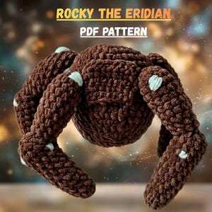 Pode incluir: Um brinquedo de aranha de crochê marrom com detalhes em azul claro nas pernas. O texto "ROCKY THE ERIDIAN PDF PATTERN" é exibido na parte superior da imagem. A aranha tem um corpo redondo e oito pernas.
