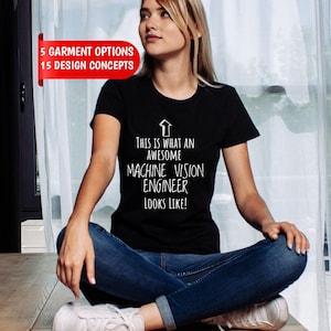 May include: A black short-sleeved t-shirt featuring a white upward-pointing arrow graphic and the text: THIS IS WHAT AN AWESOME MACHINE VISION ENGINEER LOOKS LIKE! A red banner in the upper left corner displays: 5 GARMENT OPTIONS 15 DESIGN CONCEPTS.
