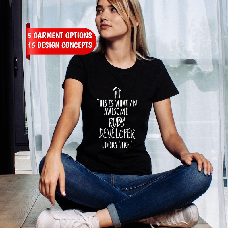 May include: A black short-sleeved t-shirt featuring a white upward-pointing arrow graphic and the text "THIS IS WHAT AN AWESOME RUBY DEVELOPER LOOKS LIKE!" A red banner in the upper left corner displays the text "5 GARMENT OPTIONS 15 DESIGN CONCEPTS".