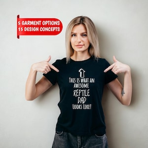 Könnte beinhalten: Ein schwarzes T-Shirt mit kurzen Ärmeln, einer weißen Pfeilgrafik nach oben und dem in Weiß aufgedruckten Text "THIS IS WHAT AN AWESOME REPTILE DAD LOOKS LIKE!". Ein rotes Banner oben links zeigt "5 GARMENT OPTIONS 15 DESIGN CONCEPTS".