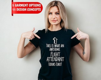 Może przedstawiać: Czarny t-shirt z krótkim rękawem, białą grafiką strzałki skierowanej w górę oraz napisem: THIS IS WHAT AN AWESOME FLIGHT ATTENDANT LOOKS LIKE! Czerwony baner w rogu zawiera tekst 5 GARMENT OPTIONS 15 DESIGN CONCEPTS.