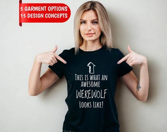 May include: A black short-sleeved t-shirt featuring a white upward-pointing arrow graphic and the text "THIS IS WHAT AN AWESOME WEREWOLF LOOKS LIKE!" in a casual font. A red banner in the top left corner displays "5 GARMENT OPTIONS 15 DESIGN CONCEPTS".