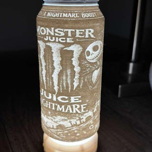 Puede incluir: L&aacute;mpara cil&iacute;ndrica marr&oacute;n con las palabras "Monster Juice" y "Juice Nightmare" grabadas en la superficie. La l&aacute;mpara presenta un dise&ntilde;o de Jack Skellington de The Nightmare Before Christmas. La l&aacute;mpara se apoya en una base de madera y emite un brillo suave.