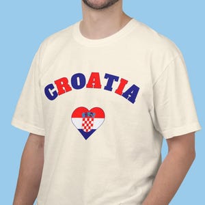 Model wearing a unisex Croatia shirt featuring a modern design with a heart-shaped Croatian flag detail on the chest. The look combines an aesthetic with a clean and minimal style. Suitable for both match days and everyday wear, this shirt offers a comfortable and versatile option for fans supporting Croatia, with a subtle yet distinctive expression of national pride.