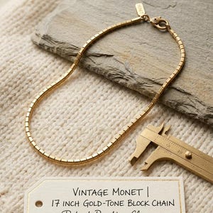 Puede incluir: Un collar de cadena de bloques en tono dorado de Monet, que mide 17 pulgadas de largo. La cadena cuenta con un cierre de langosta y una pequeña etiqueta rectangular marcada como Monet. Un calibrador de latón está cerca, y una etiqueta dice Vintage Monet 17 inch gold-tone block chain patent pending clasp.