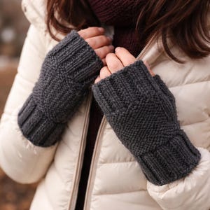 May include: Dark gray knitted fingerless gloves. The gloves are made of a thick yarn and have a ribbed cuff. The design features a textured pattern on the back of the hand. These gloves are perfect for keeping hands warm in cold weather.