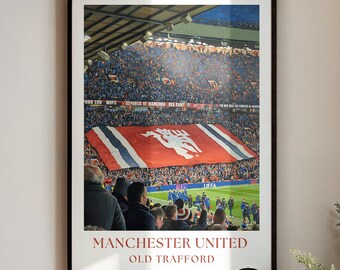 Può includere: Stampa incorniciata di una partita di calcio del Manchester United a Old Trafford. L'immagine mostra un grande striscione rosso con l'emblema della squadra e la folla sugli spalti. Il testo "MANCHESTER UNITED OLD TRAFFORD" è stampato in basso.