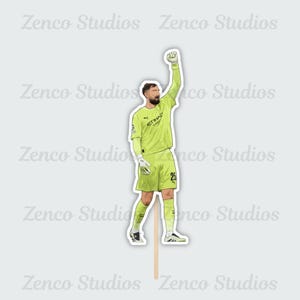 May include: A sticker featuring a cartoon illustration of a soccer goalkeeper in a light green uniform with the number 25. The goalkeeper is raising his fist in the air. The sticker has a wooden stick attached.