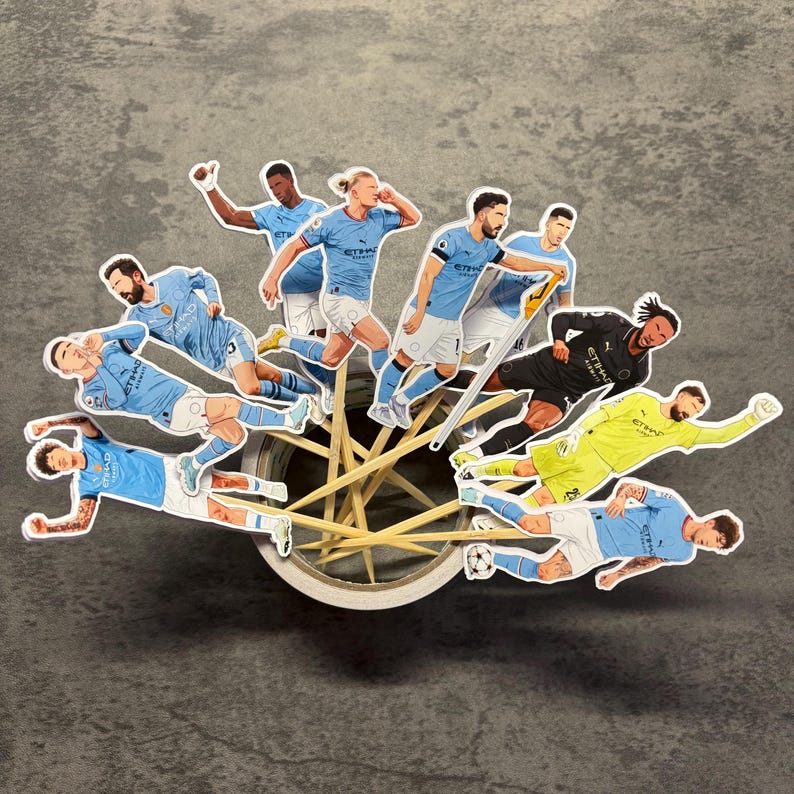 May include: A whimsical arrangement of soccer player stickers in light blue and black uniforms, seemingly propelled by a wooden wheel. The players are in various action poses, creating a dynamic and playful scene.
