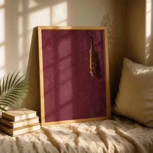 May include: A rectangular wall art piece in a light wood frame featuring a solid deep burgundy background with a small, vertical illustration of a tiger positioned in the upper right quadrant of the frame, facing downward toward the bottom.