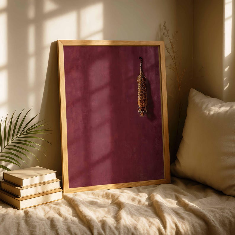 May include: A rectangular wall art piece in a light wood frame featuring a solid deep burgundy background with a small, vertical illustration of a tiger positioned in the upper right quadrant of the frame, facing downward toward the bottom.