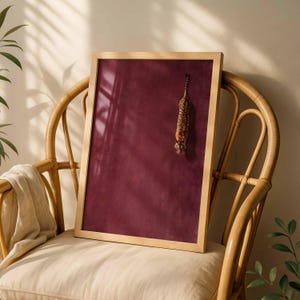 May include: A rectangular framed wall art piece featuring a deep burgundy background with a small, vertically oriented illustration of a tiger positioned in the upper right quadrant, encased in a light-toned wooden frame.