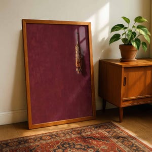 May include: A rectangular framed wall art piece featuring a deep burgundy, textured background with a small, vertical illustration of a tiger positioned in the upper right quadrant, enclosed within a light-toned wooden frame.