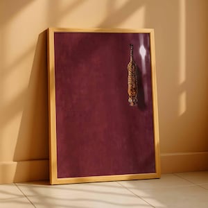 May include: A rectangular wall art print in a light wood frame featuring a tiger viewed from above, positioned on the right side against a solid deep burgundy background. The tiger has orange and black stripes and is facing downward.