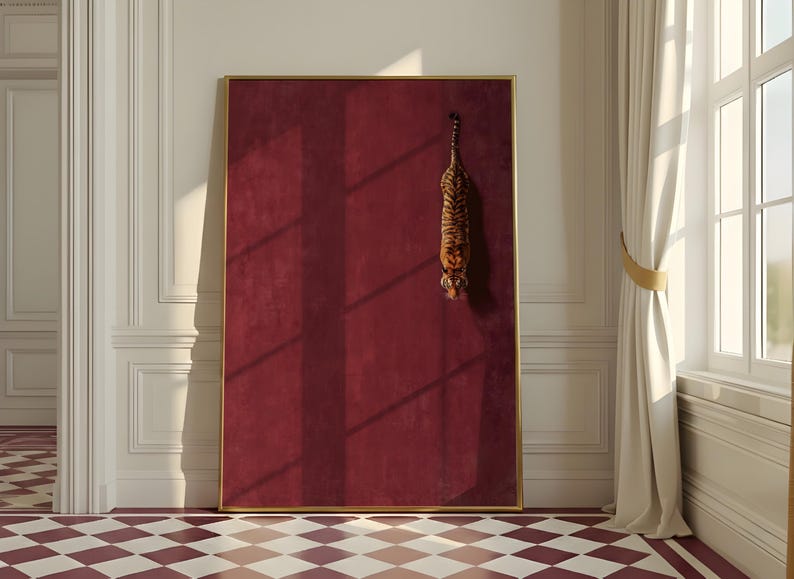 May include: A large rectangular wall art piece featuring a deep burgundy, textured background enclosed in a thin gold frame. A small, realistic tiger is depicted in a vertical, downward-facing position on the right side of the solid red surface.