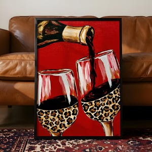 May include: A framed painting featuring a dark wine bottle pouring red wine into two stemmed glasses. The lower portions of both glasses are decorated with a brown and black leopard print pattern against a solid, vibrant red background.
